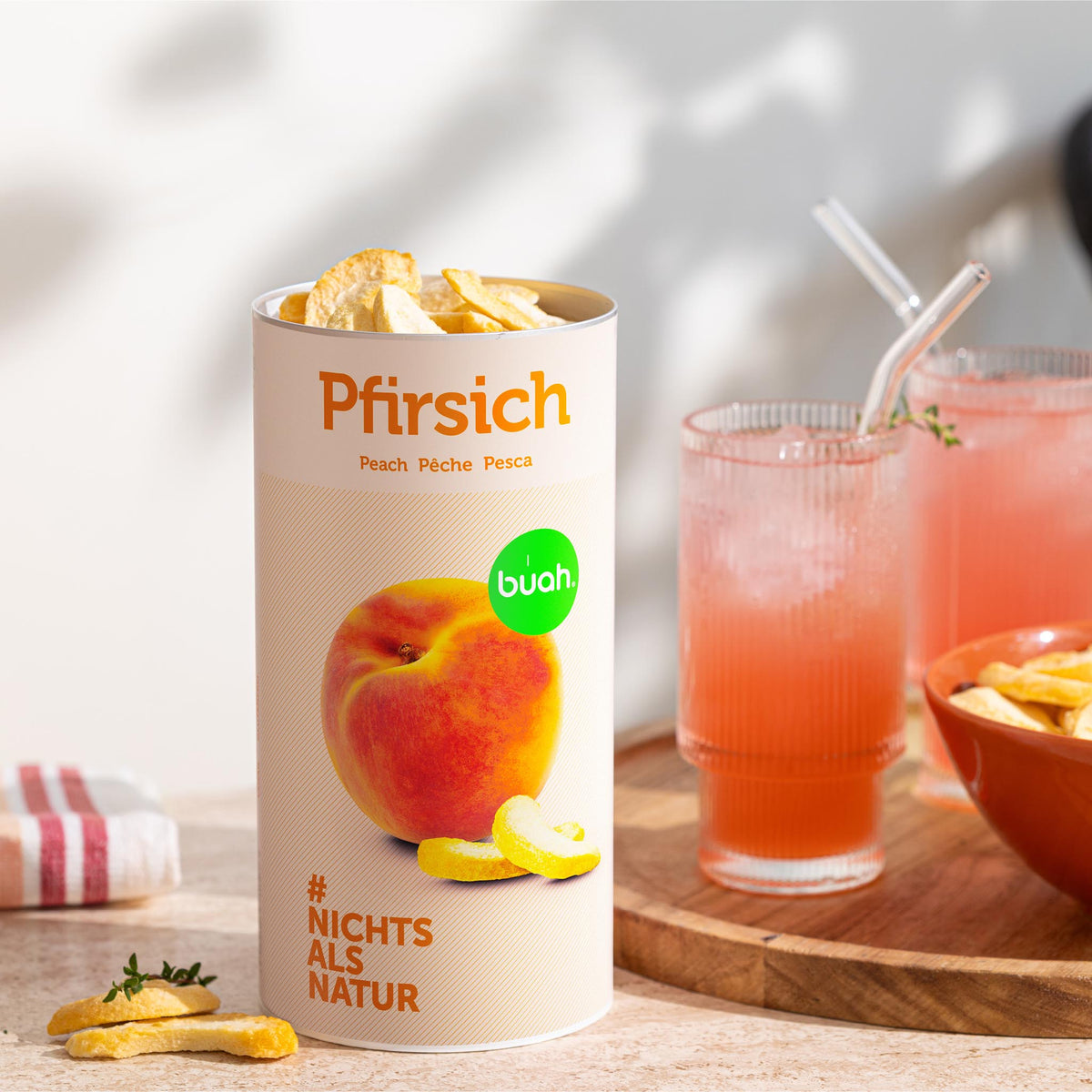 Dose buah gefriergetrockneter Pfirsich neben zwei selbst gemachten Pfirsich Eistee im Glas