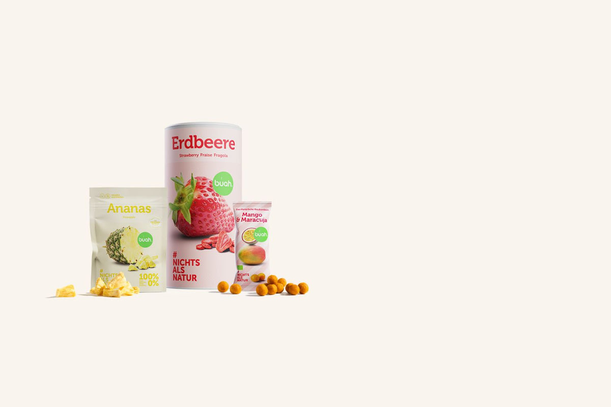 buah Icon alle Produkte mit buah grosser Dose Erdbeere, Snackpack Ananas und Kaubonbons nebeneinander stehend vor beigem Hintergrund