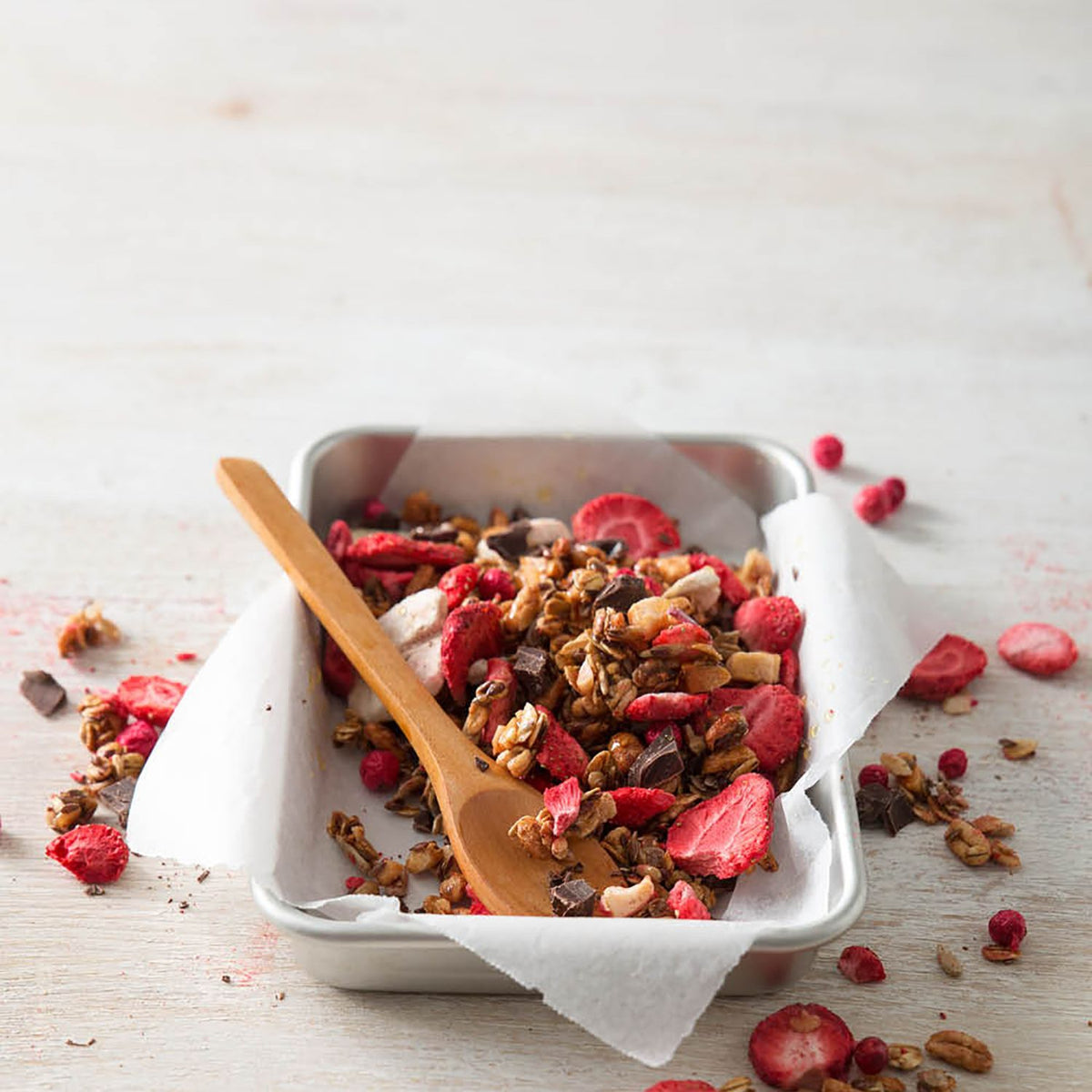 Selbstgemachtes Granola mit buah gefriergetrockneten Erdbeeren in einer flachen Schale aus Metall mit einem Holzlöffel im Granola