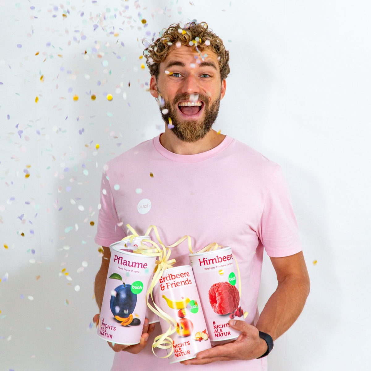 Daniel Gruender von buah in rosa buah Shirt mit buah gefriergetrockneten Fruechten in der Dose im Arm - Konfetti und Luftschlangen im Hintergrund fuer den buah Birthday
