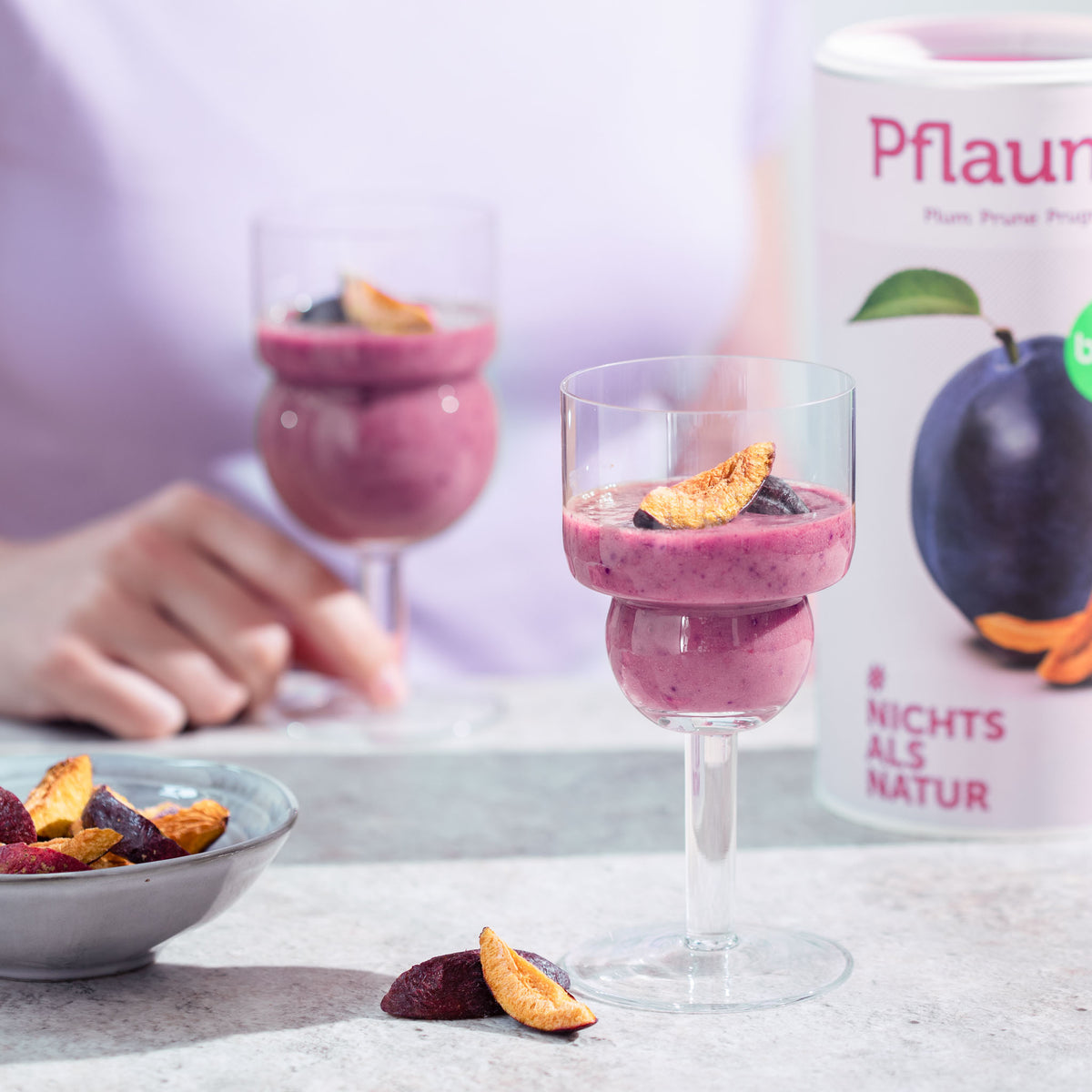 Dessertbecher mit einem Joghurt Dessert und Pflaume stehen auf einem Tisch, daneben eine Schale buah gefriergetrockneter Pflaumen und eine Dose buah Pflaume