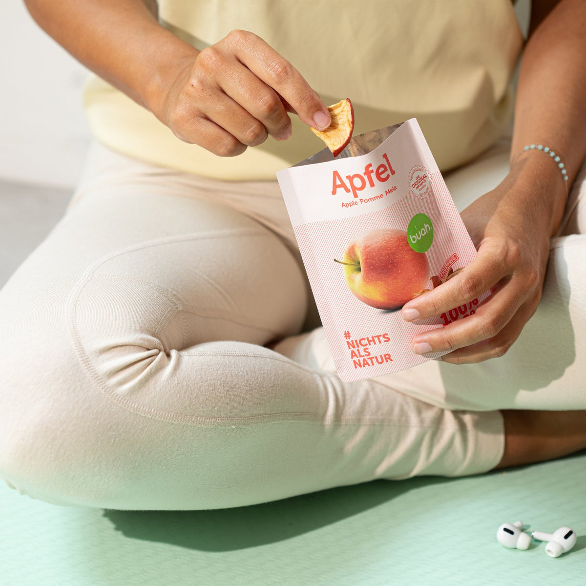 Frau in Sportsachen auf Yogamatte mit buah Snackpack Apfel isst vakuumgetrockneten Apfel