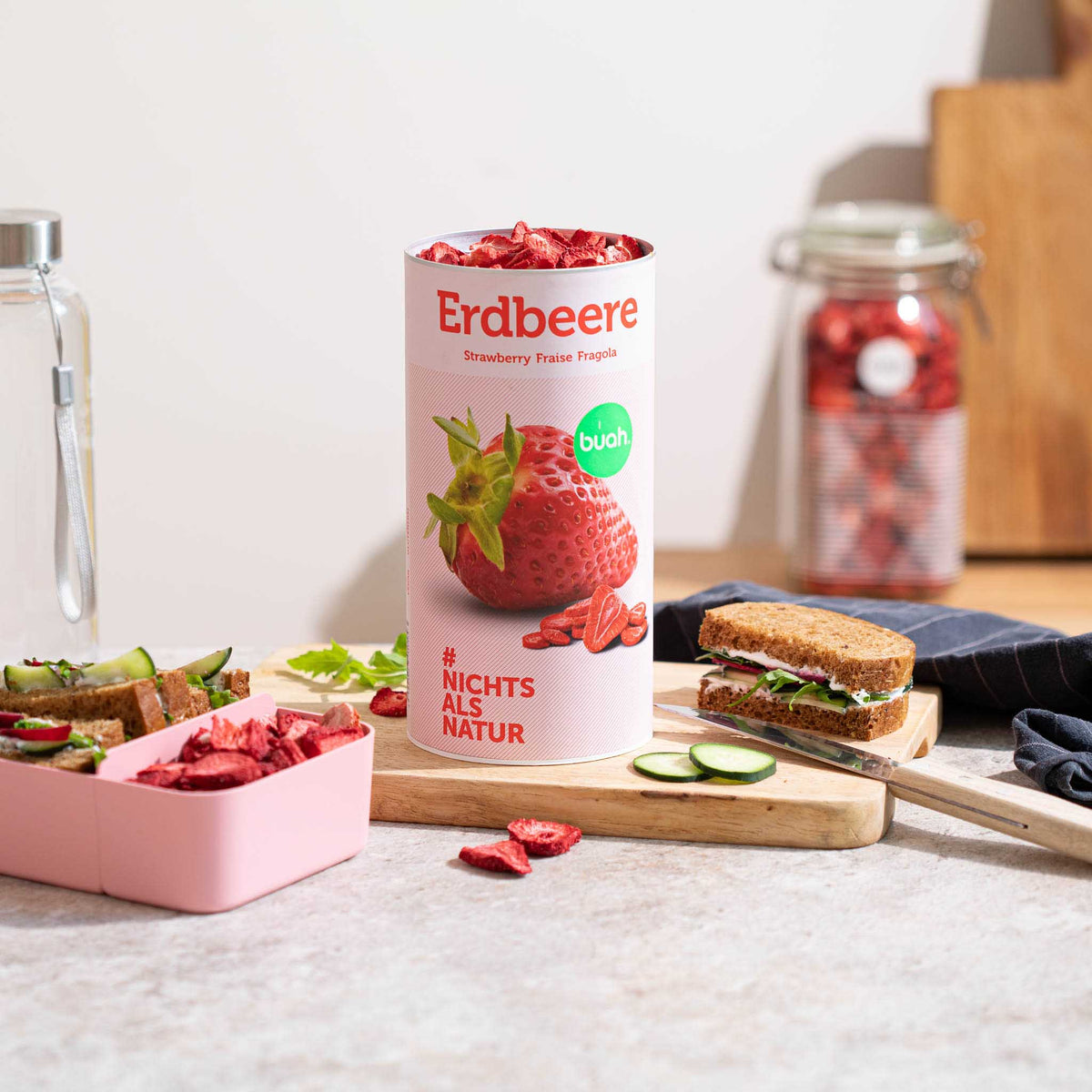 Dose buah Erdbeeren steht auf Schneidebrett neben einem Sandwich und einer Brotdose