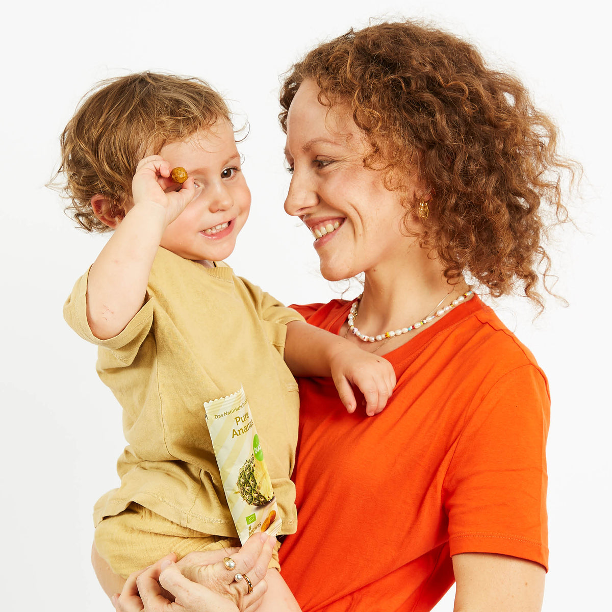 Mama mit Sohn auf dem Arm, der Ananas Kaubonbon von buah in der Hand hat