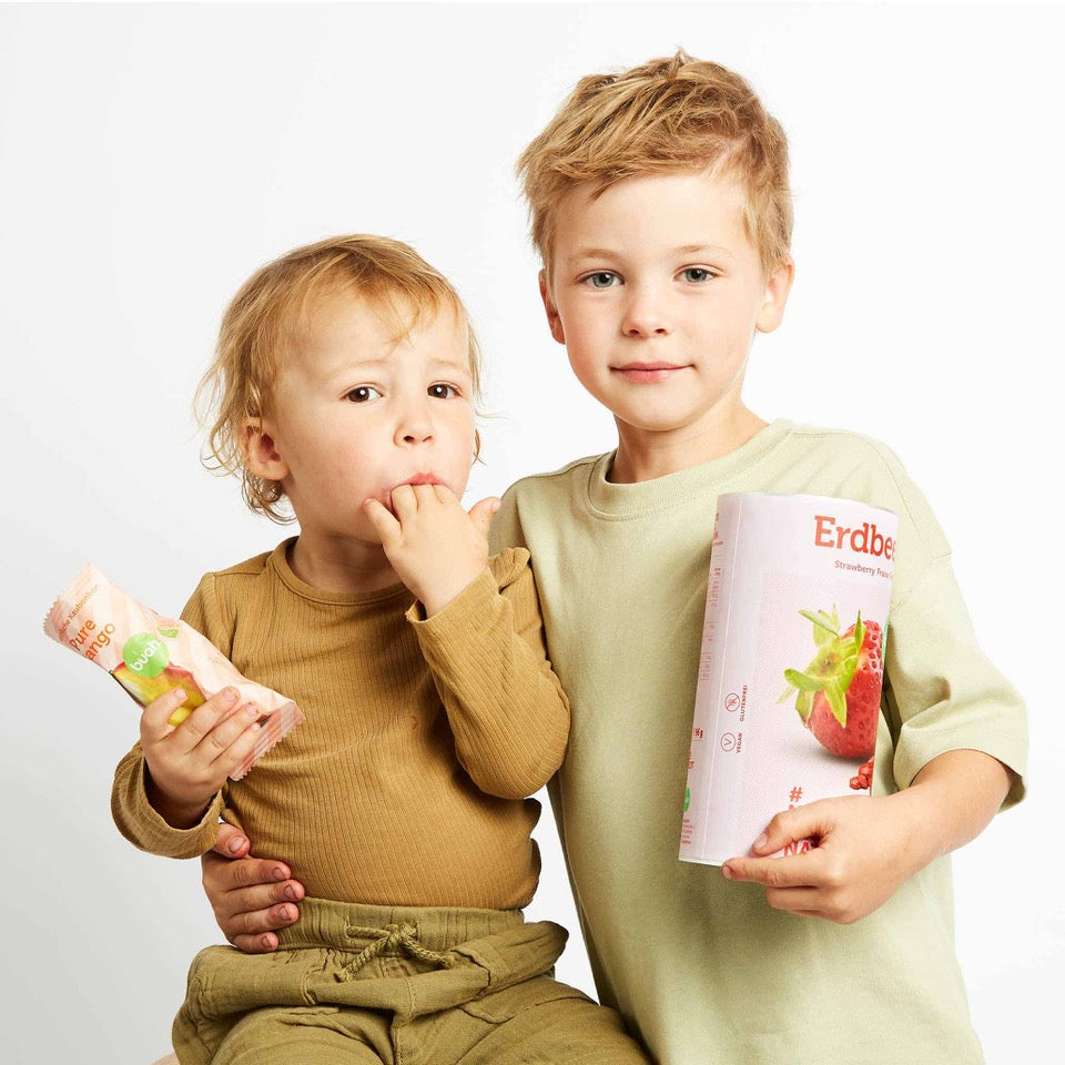 Zwei Kleinkinder umarmen sich und halten buah Erdbeeren und Kaubonbons in der Hand