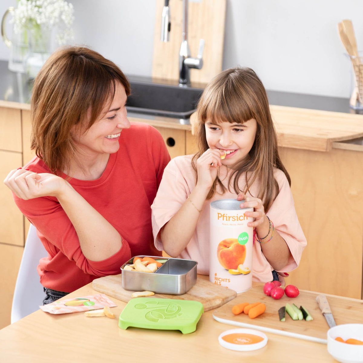 Mama und Tochter sitzen am Tisch und essen buah Pfirsich aus der Dose 