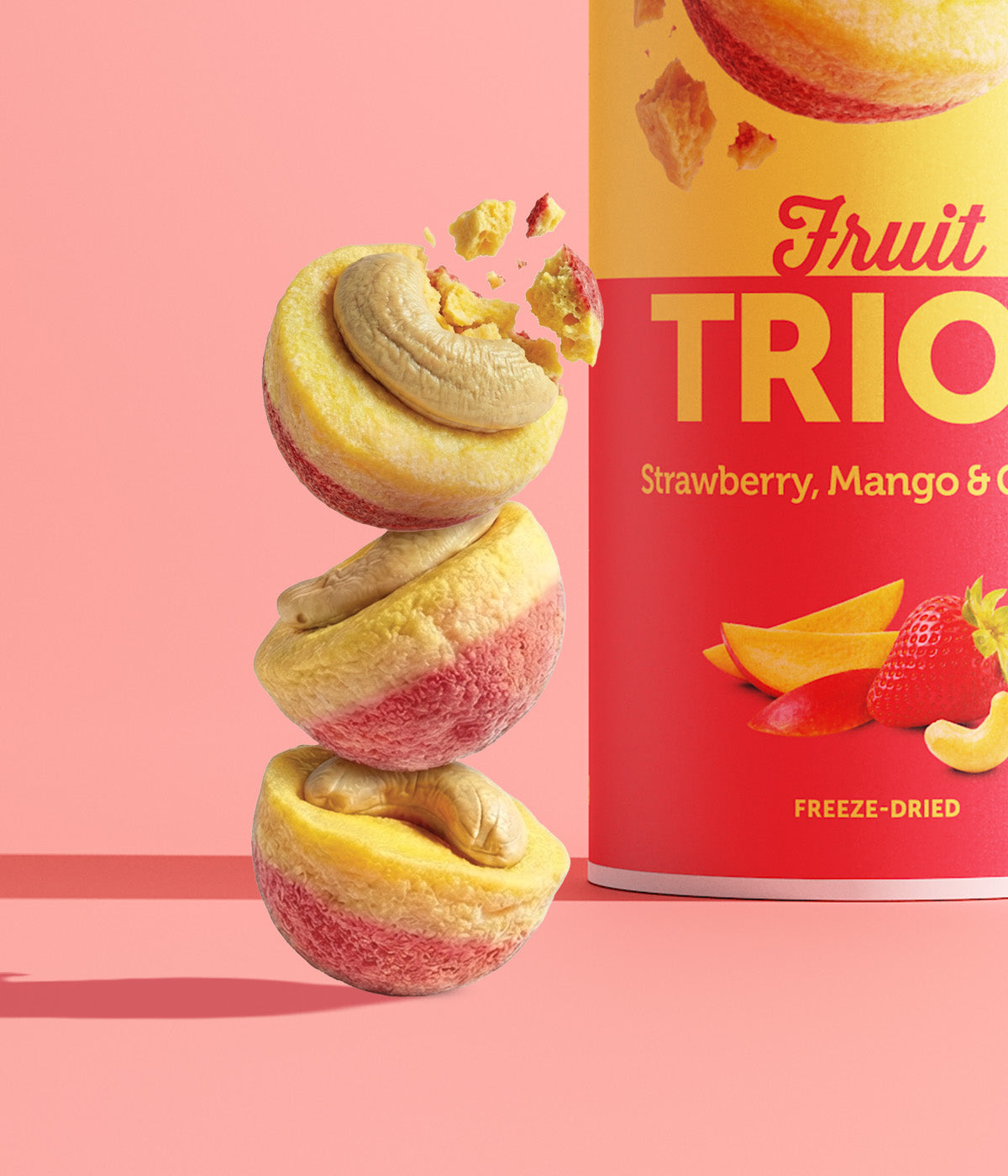 Ein Turm aus drei runden buah Fruit TRIOS Stücken der Sorte Strawberry, Mango & Cashew vor pinkem Hintergrund. Das oberste, pink-gelbe Fruchtstück zerbricht in der Luft. Auf jedem Stück liegt ein Cashewkern.